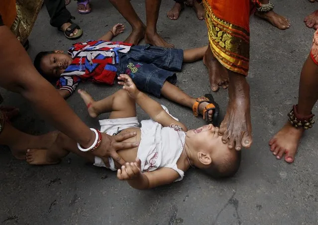 A Hindu holy man (not pictured) touches an infant with his foot as part of a ritual to bless him during a religious procession to mark the Gajan festival in Kolkata April 13, 2015. Devotees offer prayers during the month-long festival in hopes of winning the god's favour and ensuring fulfilment of their wishes, as the festival ends on the last day of the Bengali calendar year on April 14. (Photo by Rupak De Chowdhuri/Reuters)