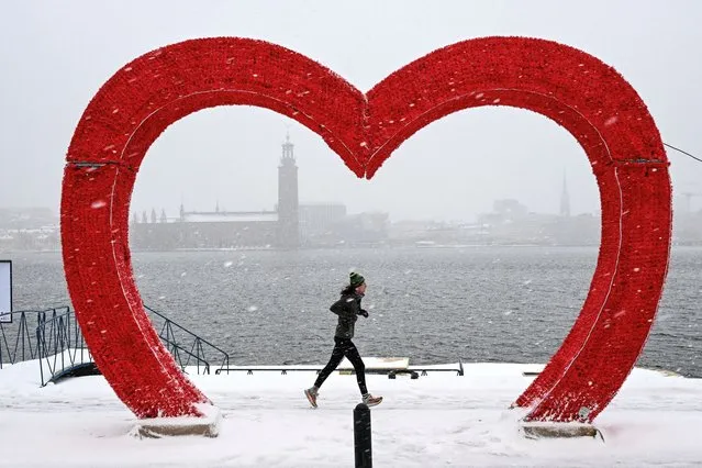 A jogger runs past a sculpture resembling a heart during snowfall in Stockholm, Sweden, on January 2, 2024, while the Stockholm City Hall is seen in the background. (Photo by Anders Wiklund/TT News Agency/AFP Photo)