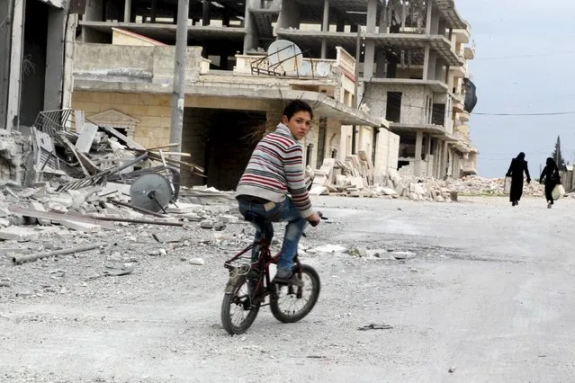 A boy rides a bicycle near damage in Kafr Hamra village, northern Aleppo countryside, Syria February 27, 2016. (Photo by Abdalrhman Ismail/Reuters)