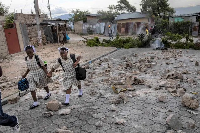Students walk hand-in-hand crossing a barricade as they head home in downtown Port-au-Prince, Haiti, Wednesday, September 22, 2021. Residents set up a barricade in protest after accusing police of killing a man during a Tuesday night raid. (Photo by Rodrigo Abd/AP Photo)