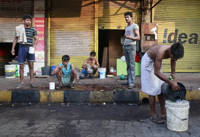 A worker cooks on a footpath as others brush their teeth at a market in Mumbai, India, March 7, 2016. (Photo by Danish Siddiqui/Reuters)
