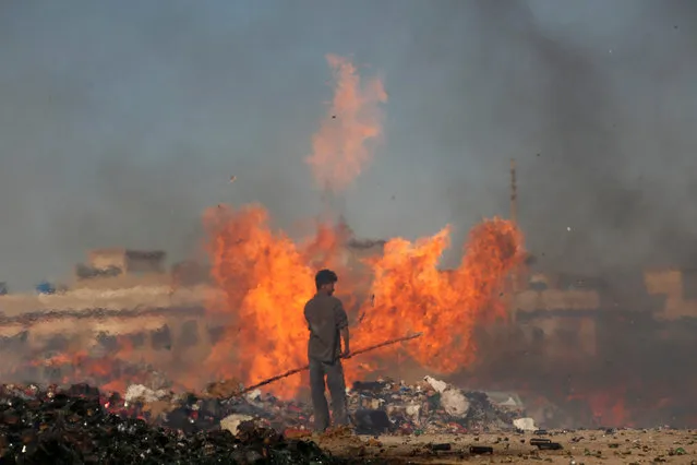 Pakistani customs employee stands amid burning piles of confiscated contraband and narcotics destroyed during a campaign marking International Customs Day in Karachi, Pakistan January 26, 2017. (Photo by Akhtar Soomro/Reuters)