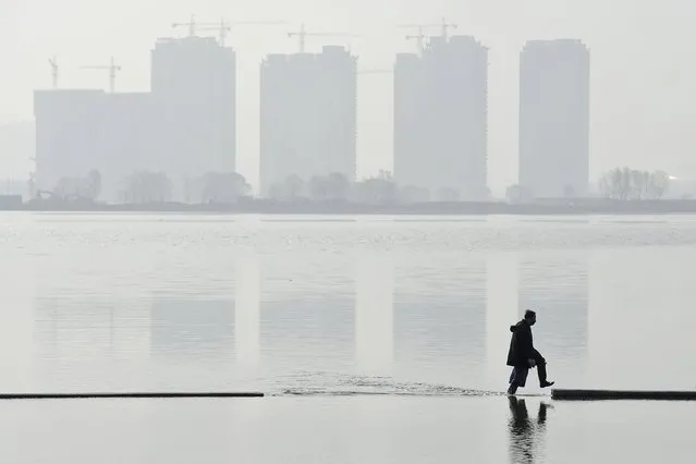 A man walks in an artificial lake near residential buildings in Taiyuan, Shanxi Province, China, March 29, 2016. (Photo by Jon Woo/Reuters)