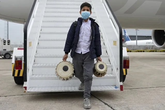 An Afghan boy carrying musical instruments disembarks from an airplane at Lisbon military airport, Monday, December 13, 2021. A group of 273 students, faculty members and their families from the Afghanistan National Institute of Music arrived Monday in Portugal, where they are being granted asylum and where they hope to rebuild their acclaimed school. (Photo by Armando Franca/AP Photo)