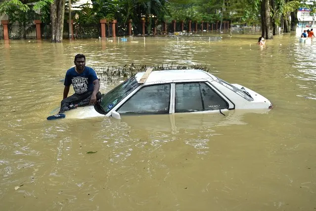 A man sits on the bonnet of a car as he waits to be evacuated by a rescue team in Shah Alam, Selangor on December 20, 2021, as Malaysia faces some of its worst floods for years. (Photo by Arif Kartono/AFP Photo)