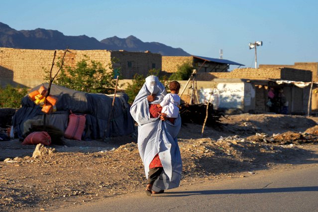 An Afghan burqa-clad woman holding a child, walks along a road on the outskirts of Kandahar on May 6, 2024. (Photo by Sanaullah Seiam/AFP Photo)