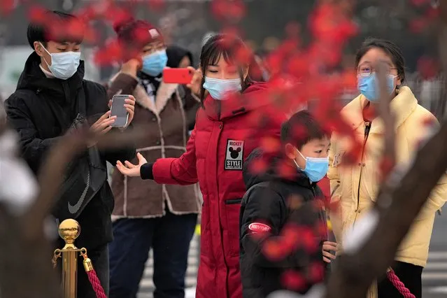 Visitors wearing face masks to help protect from the coronavirus gather to take souvenir photo with a decoration for the Lunar New Year at Qianmen Street, a popular tourist spot in Beijing, Sunday, January 23, 2022. (Photo by Andy Wong/AP Photo)