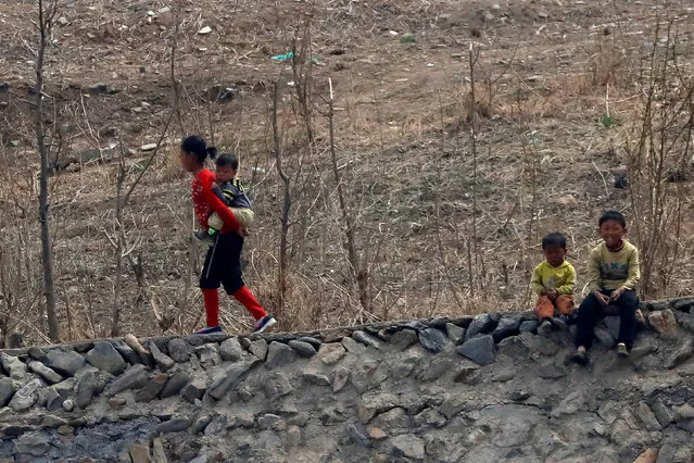 A North Korean girl carries an infant on her back while two children sit on a ledge on the banks of the Yalu River in Sinuiju, North Korea, which borders Dandong in China's Liaoning province, April 16, 2017. (Photo by Aly Song/Reuters)