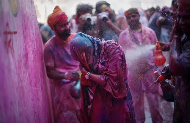 A girl covers herself as she is sprayed with coloured water during the religious festival of Holi inside a temple in Nandgaon village, in the state of Uttar Pradesh, India, March 12, 2022. (Photo by Adnan Abidi/Reuters)