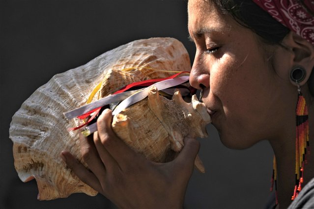 A woman plays a shell musical instrument on the 11th anniversary of the murder of Daniel Zamudio, a gay youth, at Zamudio's gravesite inside the General Cemetery where the Integration and Homosexual Liberation movement added six symbolic tombstones to represent recent victims of discrimination in Santiago, Chile, Monday, March 27, 2023. Zamudio was attacked in 2012 for being homosexual and died after 25 days in a coma, inspiring the “Zamudio Law” against the crimes of homophobia, transphobia and any other type of discrimination. (Photo by Esteban Felix/AP Photo)