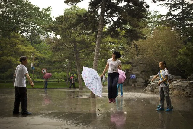 In this Sunday, May 17, 2015 photo, a girl holds an umbrella as she skips rope during a rain shower at a park in Beijing. (Photo by Mark Schiefelbein/AP Photo)