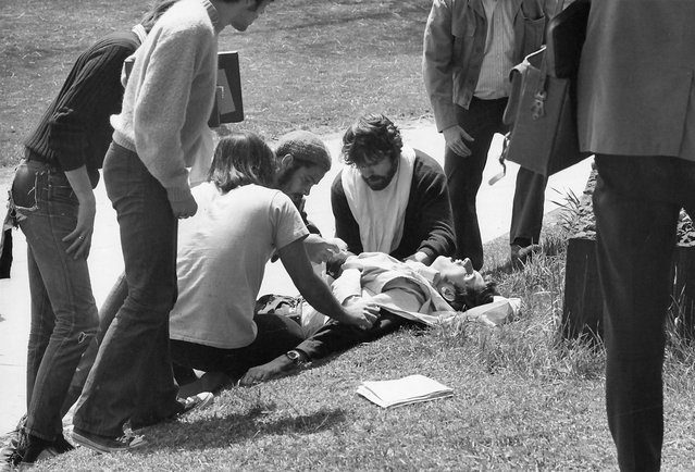 Kent State University student Joe Cullum (center, with beard) and others kneel on the grass beside wounded fellow student John Clearly after the latter had been shot when the Ohio National Guard opened fire on antiwar protestors, Kent, Ohio, May 4, 1970. Four protestors were shot and killed (and nine injured) during the incident. A cropped version of this image appeared in the cover of the May 15, 1970, issue of Life magazine. (Photo by Howard Ruffner/Getty Images)