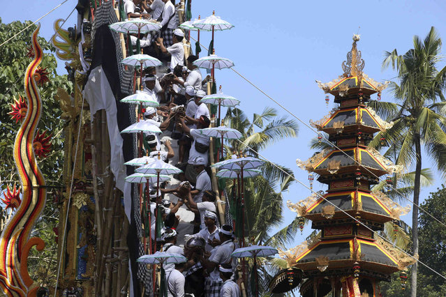 Men put the remains of their deceased relatives into a tower during traditional mass cremation called ''ngaben'' on Wednesday, August 14, 2024, in Manggis, Bali, Indonesia. (Photo by Firdia Lisnawati/AP Photo)