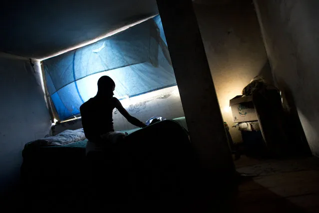 In this June 29, 2015 photo, electrician Jimmy Bellefleur, 35, sits on his bed in the room his family occupies inside an abandoned, earthquake damaged government office building in Port-au-Prince, Haiti. Before the quake, his family lived in two rented rooms, but the building was destroyed, Bellefleur said, and they lived on the streets for more than a year before finding their current home. “I don't have the means to leave”, he said. (Photo by Rebecca Blackwell/AP Photo)