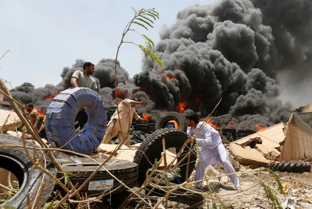 Workers move tires from a warehouse after a fire broke out at an industrial zone in Karachi, Pakistan June 24, 2016. (Photo by Akhtar Soomro/Reuters)