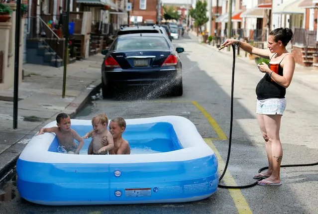Alexis Denaro sprays water into a inflatable pool as her sons, from right to left, Dominic Denaro, 8, William Giangrante, 5 and Lorenzo Giangrante, 2, cool off along the 2500 block of Darien Street, Friday, July 21, 2017, in the South Philly neighborhood of Philadelphia. (Photo by Yong Kim/The Philadelphia Inquirer via AP Photo)