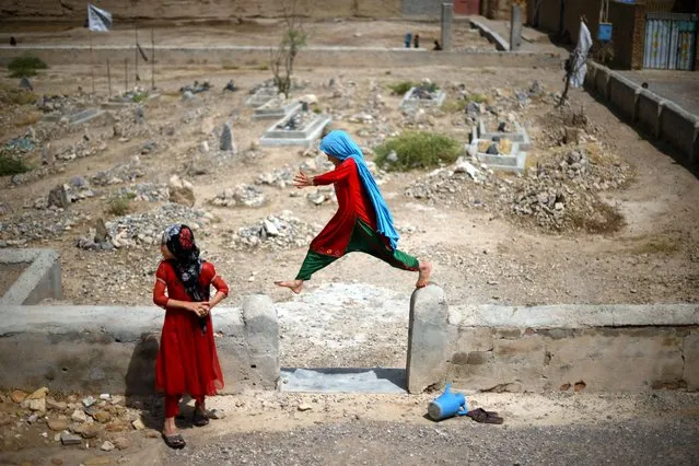 An Afghan girl jumps off the wall of a small cemetery in Kandahar on July 29, 2022. (Photo by Daniel Leal/AFP Photo)