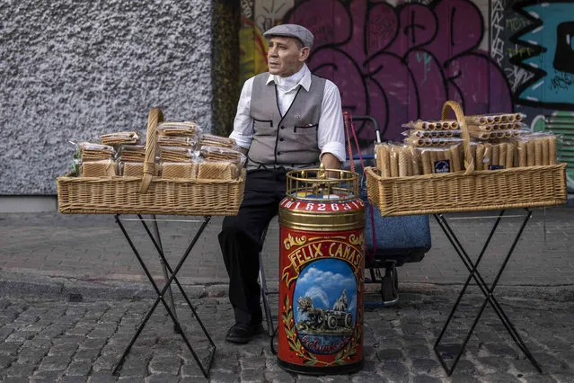 A wafer-sellers known as barquillero waits for customers during the festivities of San Cayetano, the patron saint of labor and bread, at the Lavapies neighbourhood in Madrid, Spain, Friday, August 5, 2022. The San Cayetano festival marks the beginning of a series of popular festivals in Madrid. (Photo by Manu Fernandez/AP Photo)