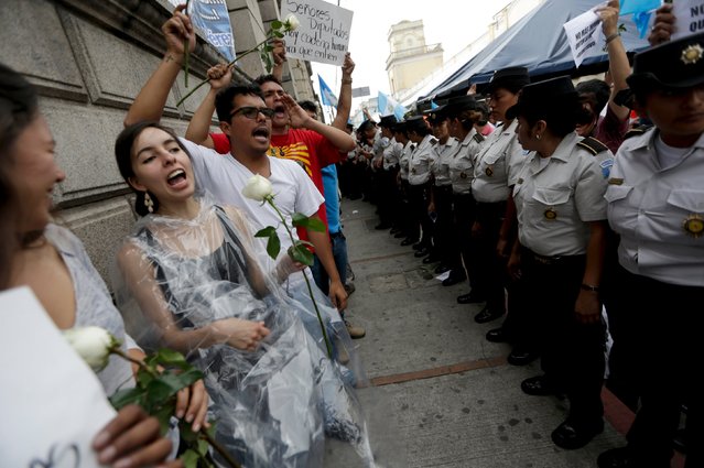 Demonstrators yell slogans as they stand in front of policemen guarding the Congress, where lawmakers wait for a session to decide if Guatemalan President Otto Perez Molina is to be stripped of his presidential immunity in Guatemala City, September 1, 2015. Guatemala's Congress was expected to vote on Tuesday on whether to strip President Perez of immunity, which would pave the way for prosecutors to charge him in a graft scandal that has engulfed his government. (Photo by Jorge Dan Lopez/Reuters)