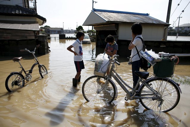 Members of a family stand in front of their home at a residential area flooded by the Kinugawa river, caused by typhoon Etau, at Araigi town in Joso, Ibaraki prefecture, Japan, September 12, 2015. (Photo by Issei Kato/Reuters)