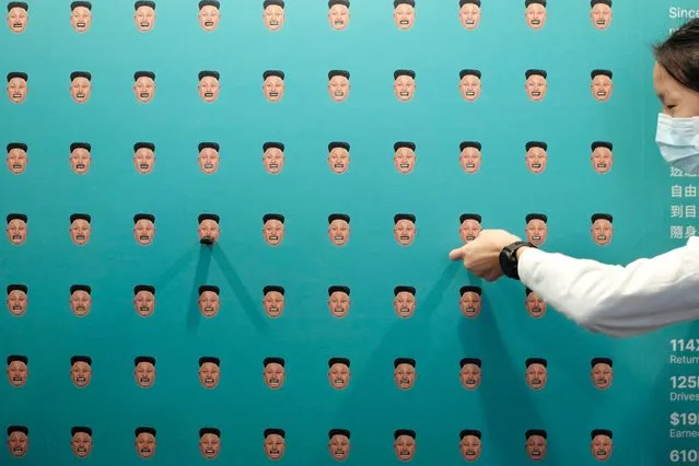 A woman plugs a USB media device containing freedom-related content into a socket on a wall depicting multiple heads of North Korean leader Kim Jong Un during the Oslo Freedom Forum in Taipei on November 3, 2022. (Photo by Sam Yeh/AFP Photo)