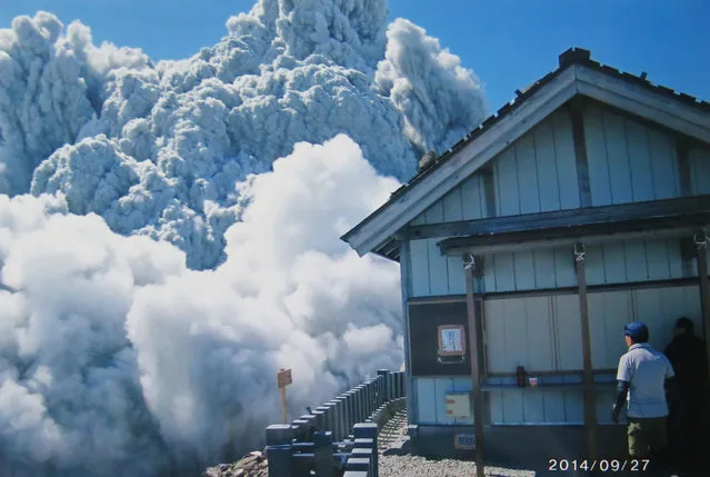 In this Saturday, September 27, 2014 file photo taken by 59-year-old hiker Izumi Noguchi who fell victim to the eruption of Mount Ontake, and was offered to Kyodo News by his wife, Hiromi, Friday, October 3, a hiker standing on the summit shrine compound on Mount Ontake watches dense plumes of gases and ash billowing from the crater as the volcanic mountain starts to erupt in central Japan. (Photo by Izumi Noguchi/AP Photo/Kyodo News)