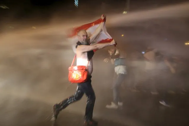 A protester carries a Lebanese flag while sprayed with water from a police water cannon in Martyr square, downtown Beirut, Lebanon October 8, 2015. (Photo by Aziz Taher/Reuters)