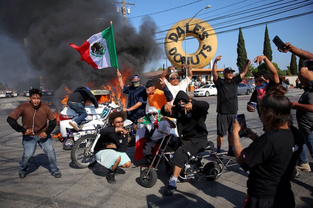 People hold Mexican flags and gesture next to a car in flames following multiple detentions by ICE, in the Los Angeles County city of Compton, California, U.S., June 7, 2025. (Photo by Daniel Cole/Reuters)