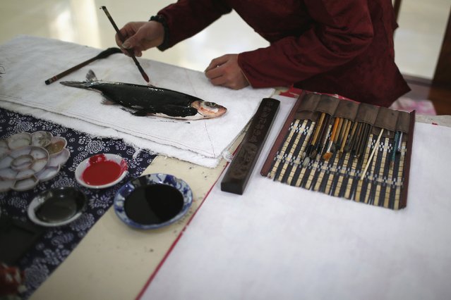 Folk artist Han Xiaoming demonstrates block printing with a live fish in Hangzhou, Zhejiang province December 4, 2014. (Photo by Aly Song/Reuters)