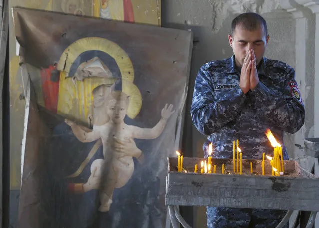 A policeman prays in the Holy Savior Cathedral, damaged by shelling by Azerbaijan's artillery during a military conflict in Shushi, the separatist region of Nagorno-Karabakh, Saturday, October 24, 2020, with a damaged icon of the Virgin on the left. The heavy shelling forced residents of Stepanakert, the regional capital of Nagorno-Karabakh, into shelters, as emergency teams rushed to extinguish fires. Nagorno-Karabakh authorities said other towns in the region were also targeted by Azerbaijani artillery fire. (Photo by AP Photo/Stringer)