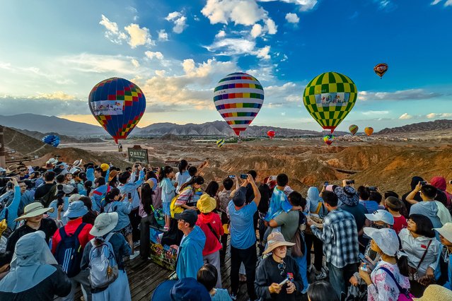 Visitors watch hot air balloons flying over Danxia landform in the Qicai Danxia Scenic Area, also known as Colorful Danxia Scenic Spot, at Zhangye National Geopark on July 31, 2025 in Zhangye, Gansu Province of China. (Photo by Kong Lingsheng/VCG via Getty Images)