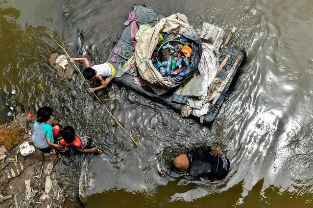 A scavenger (R) searches for valuable waste to resale as children (L) play next to him in a dirty river in Jakarta on March 21, 2018. (Photo by Bay Ismoyo/AFP Photo)