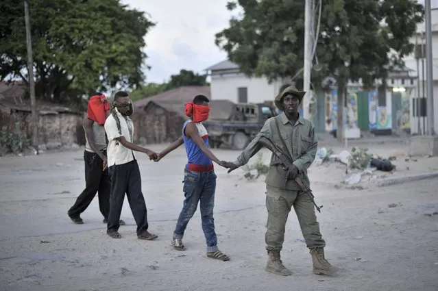This handout photo released by the AU-UN 1ST shows three young men led by a member of the Somali Police Force to a holding area with other civilians during an operation aimed at improving security in Mogadishu, Somalia, on May 21. AMISOM, in support of the Somali Police Force, last night cordoned off one square kilometer in the Wardhiigleey district of Mogadishu in an attempt to weed out members of the extremist group, al Shabaab. Many of the area's young men were temporarily detained by the SPF and then screened in order to determine whether they had any links to the group. (Photo by Tobin Jones/AU-UN IST via Reuters)