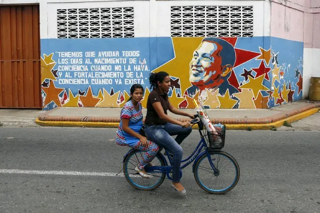 Women ride past a mural depicting late Venezuela's President Hugo Chavez in front of his childhood house, in Sabaneta, in the state of Barinas, November 19, 2015. Venezuela's United Socialist Party is ailing ahead of a Dec. 6 legislative election, including in Sabaneta, late leader Hugo Chavez's sleepy hometown in the middle of the country's agricultural heartland. (Photo by Marco Bello/Reuters)