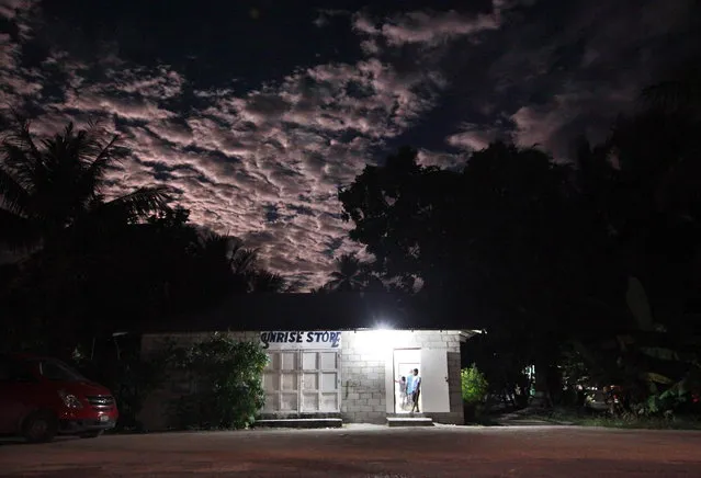 A full moon rises as a young boy stands in the doorway of a shop called the Sunrise Store located in the village of Ambo located on South Tarawa in the central Pacific island nation of Kiribati May 25, 2013. (Photo by David Gray/Reuters)