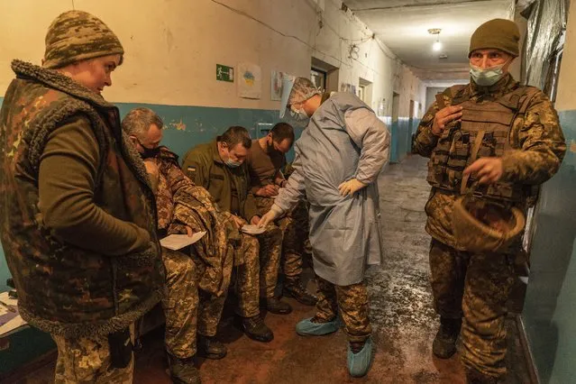 A Ukrainian military medic helps Ukrainian servicemen to fill in a medical form before receiving a dose of the AstraZeneca COVID-19 vaccine marketed under the name CoviShield at a military base near the front-line town of Krasnohorivka, eastern Ukraine, Friday, March 5, 2021. The country designated 14,000 doses of its first vaccine shipment for the military, especially those fighting Russia-backed separatists in the east. But only 1,030 troops have been vaccinated thus far. In the front-line town of Krasnohorivka, soldiers widely refuse to vaccinate. (Photo by Evgeniy Maloletka/AP Photo)