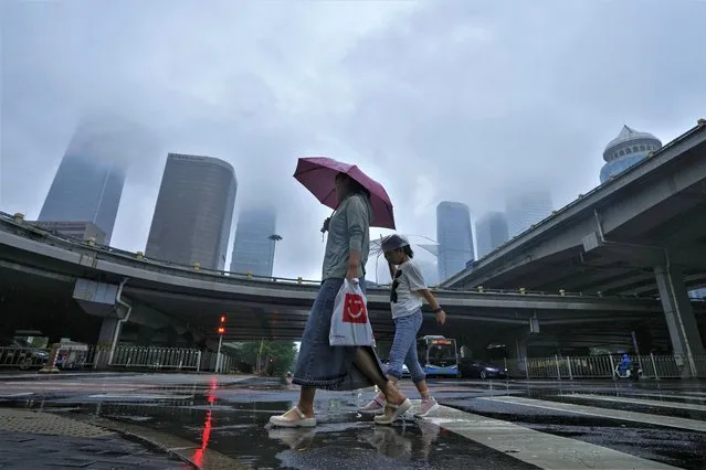 A woman and a child use umbrellas to protect themselves from rainfall brought about by tropical storm as they walk by Central Business District in Beijing, Tuesday, August 1, 2023. Chinese state media report some have died and others are missing amid flooding in the mountains surrounding the capital Beijing. (Photo by Andy Wong/AP Photo)
