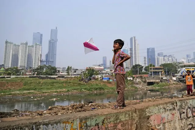 A boy plays with a kite as the city skyline is seen in the background in Jakarta, Indonesia, Friday, August 11, 2023. (Photo by Dita Alangkara/AP Photo)