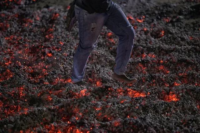 A man walks barefoot across a bed of burning coals during the traditional Sao Joao prayer, performed by the Quilombola community of Mato do Ticao, in Jaboticatubas, Minas Gerais State, Brazil, on the night of June 23-24, 2022. At exactly midnight, the faithful spread the embers of the bonfire and, as is the religious custom, walk barefoot across a bed of burning coals. (Photo by Douglas Magno/AFP Photo)