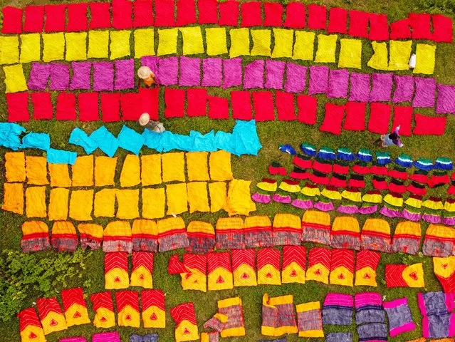 Hundreds of pieces of dyed cloth are spread out across a field at Batik Village in Narayanganj, Bangladesh on September 3, 2023 for drying which looks like a Kingdom of Colors. Workers use hats for protection from the scorching heat because they have to constantly turn the colorful fabrics so that they dry perfectly in the sunlight. Beautifully embellished colorful cloths are created using the Indonesian technique called “Batik”. Parts of the design are blocked out by applying hot wax over them, then a dye is applied on top and the parts covered in wax resist the dye and remain the original color. About 1,500 pieces of cloth are laid to dry here every day. The process usually takes two hours, with each set of 350 pieces at a time to dry in temperatures that can reach over 36 degrees Celsius. The colorful cloths which sell for less than $3 (3 USD) are arranged on patches of grass to dry out completely as it is cheaper and more sustainable to dry them out in sunlight. Once the fabrics are dried, they are made into garments and sold worldwide. (Photo by Joy Saha/ZUMA Press Wire/EPA/EFE/Rex Features/Shutterstock)