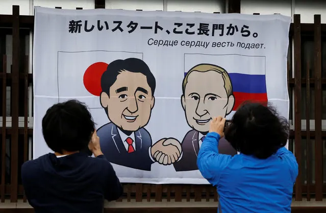 People take photos of a banner showing Japan's Prime Minister Shinzo Abe and Russian President Vladimir Putin at the Senzaki station in Nagato, Yamaguchi prefecture, Japan, December 14, 2016, a day before their summit meeting. The words on top reads, “A new start from here in Nagato”. (Photo by Toru Hanai/Reuters)