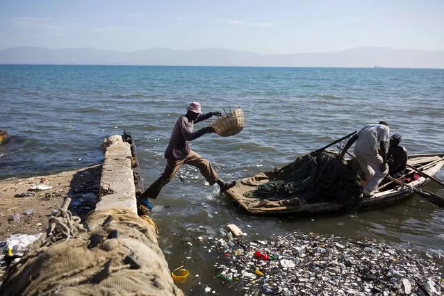 In this August 13, 2018 photo, a fisherman jumps on to his wooden boat, joining his mates as they head out to the sea from Port-au-Prince, Haiti. (Photo by Dieu Nalio Chery/AP Photo)