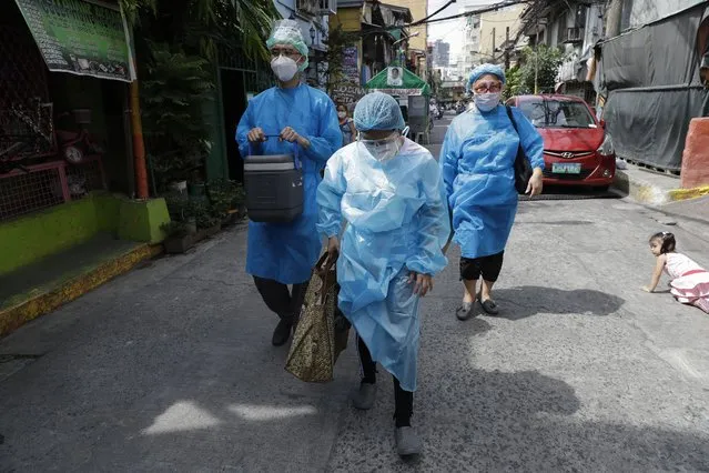 Health workers in protective suits walk to the homes of residents who are not able to go to vaccination centers in Manila, Philippines on Wednesday, May 19, 2021. Philippine President Rodrigo Duterte has eased a lockdown in the bustling capital and adjacent provinces to fight economic recession and hunger but has still barred public gatherings this month, when many Roman Catholic festivals are held. (Photo by Aaron Favila/AP Photo)