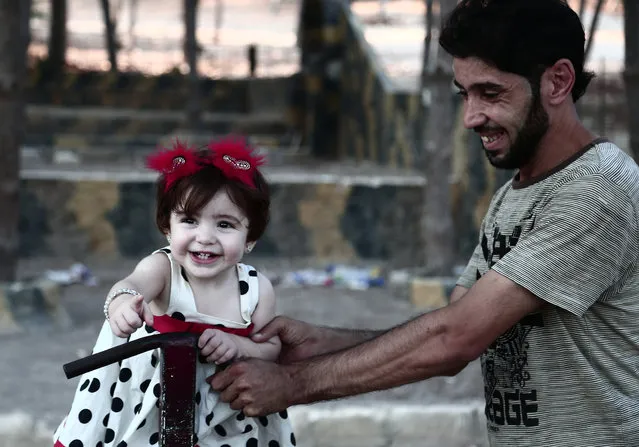 A man plays with a child dressed in her holiday clothes on the second day of Eid el-Adha at a park in the Syrian city of Afrin on August 22, 2018. Displaced from their homes in Syria's Eastern Ghouta, families sought refuge in abandoned houses in the traditionally Kurdish town of Afrin earlier this year. (Photo by Nazeer Al-Khatib/AFP Photo)