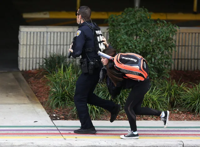 A young woman runs behind a police officer as they seek cover outside of Fort Lauderdale-Hollywood International airport after a shooting took place near the baggage claim on January 6, 2017 in Fort Lauderdale, Florida. Officials are reporting that five people wear killed and eight wounded in an attack from a single gunman.  (Photo by Joe Raedle/Getty Images)