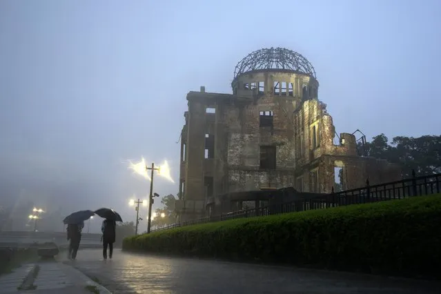 In this July 15, 2021, file photo, men walk in a heavy rain near the Atomic Bomb Dome in Hiroshima, western Japan. Japanese Prime Minister Yoshihide Suga said Monday, July 26, 2021, that he has decided to recognize 84 Hiroshima residents who were exposed to highly radioactive “black rain” just after the  U.S. atomic bombing as “hibakusha" eligible for official medical support. (Photo by Eugene Hoshiko/AP Photo/File)