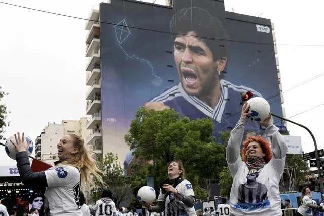 Women toss around soccer balls during the inauguration of a mural of Diego Maradona by artist Martin Ron, in Buenos Aires, Argentina, Sunday, October 30, 2022. The massive artwork, 148 feet high and 131 feet wide (45 meters by 40 meters) and painted on the side of a 14-story building, is one of several tributes that Argentines have dedicated to their soccer “God” shortly before the start of this year's World Cup in Qatar, the first since Maradona's death on Nov. 25, 2020. (Photo by Rodrigo Abd/AP Photo)