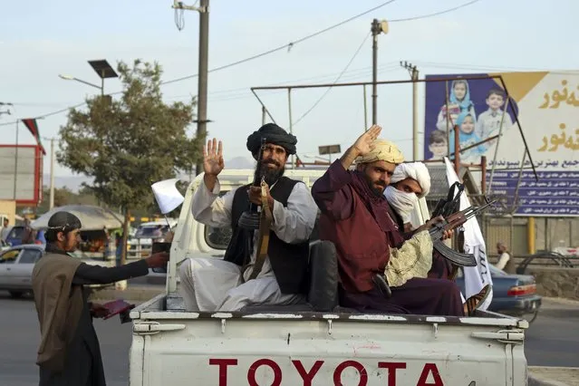 Taliban fighters wave from the back of a pickup truck, in Kabul, Afghanistan, Monday, August 30, 2021. Many Afghans are anxious about the Taliban rule and are figuring out ways to get out of Afghanistan. But it's the financial desperation that seems to hang heavy over the city. (Photo by Khwaja Tawfiq Sediqi/AP Photo)