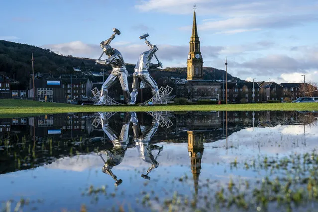The Shipbuilders of Port Glasgow sculpture in Coronation Park, Inverclyde, is reflected in large puddles after heavy downpours, in Port Glasgow, Scotland, Friday January 5, 2024. The impact of surface water and river flooding will continue to be “significant” across parts of the country following heavy rainfall, experts have warned. (Photo by Jane Barlow/PA Wire via AP Photo)