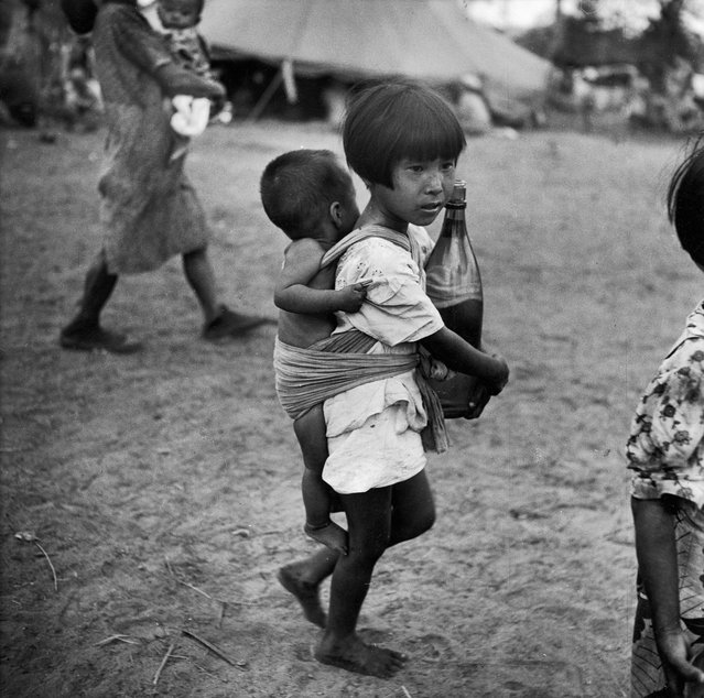 Little Japanese girl in village on Saipan carrying a big bottle of water in her arms and a baby on her back, 1944. (Photo by W. Eugene Smith/The LIFE Picture Collection/Getty Images)